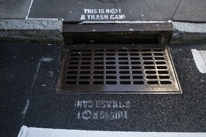Stencil signage that reads 'THIS IS NOT A TRASH CAN' over sewers on Febraury 5th, 2022 in New York City.